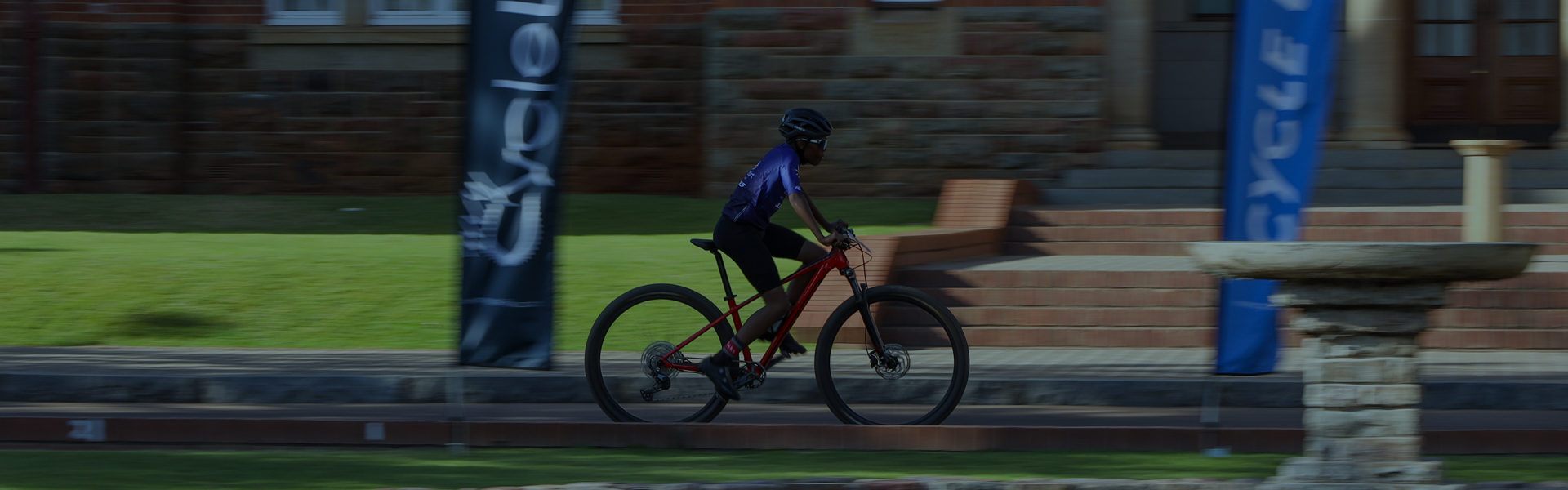 A rider racing past a school building and Cycle Lab flags